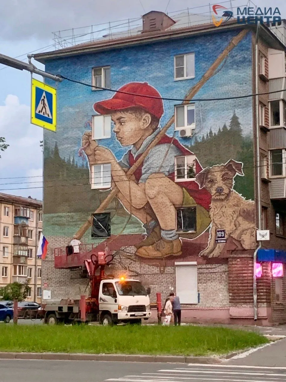 На доме по улице Ленина в Череповце появился крупный мурал с изображением мальчика-рыбака. Художники нанесли картину поверх жилых окон — издалека это создает эффект «сквозных дыр» и вызывает тревожные ассоциации. При этом изменения фасада требуют согласия собственников.